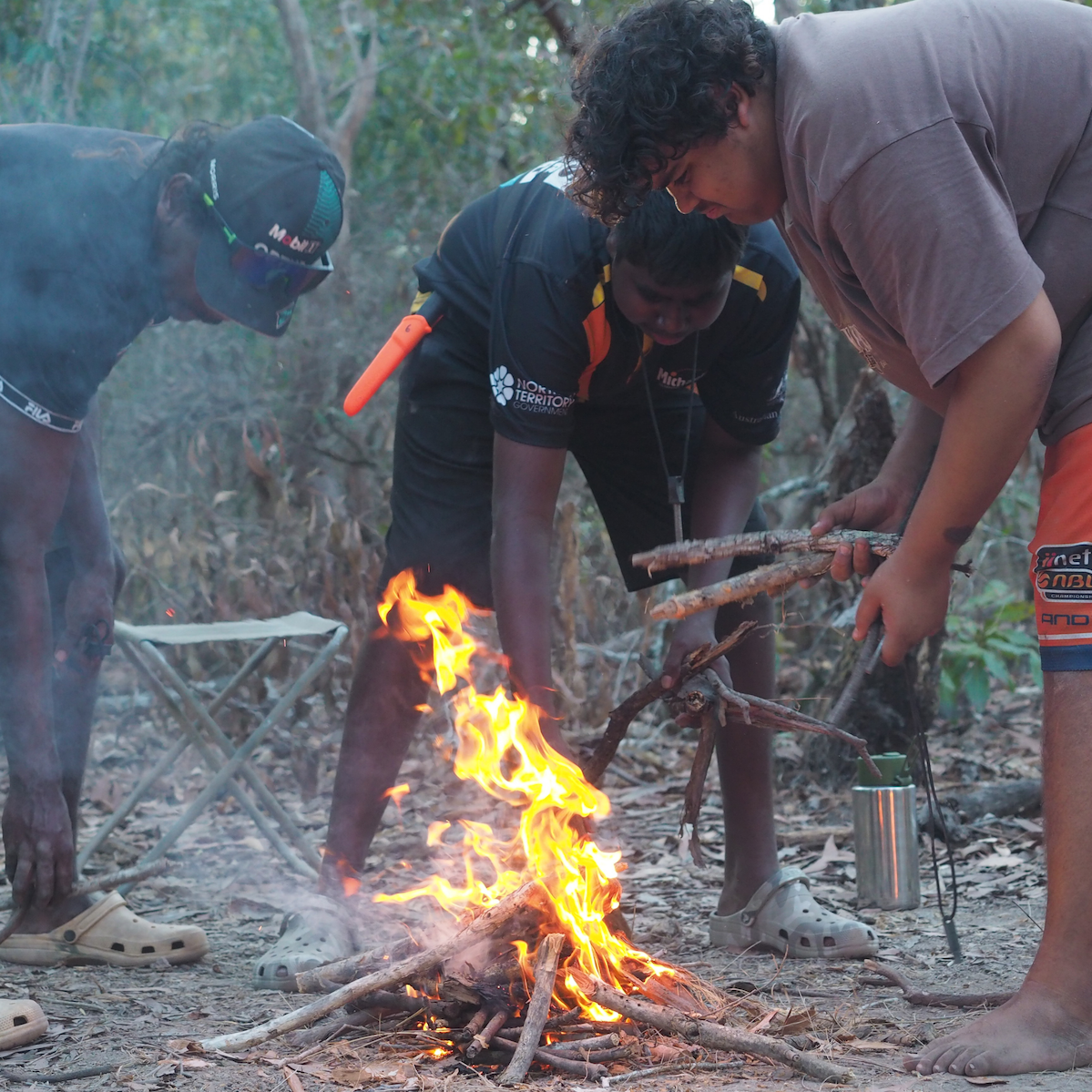 Young people tending a small campfire, learning bushcraft skills in the bush.